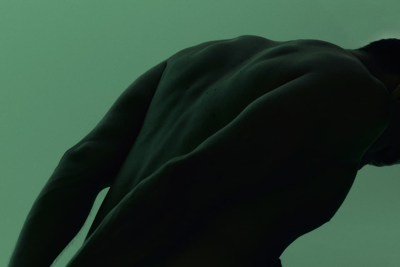Shoulders and back in warm green light, evoking physicality and vitality